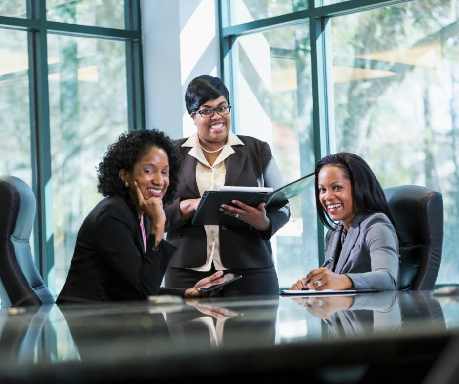 Three businesswomen sitting around a conference table and smiling towards the camera