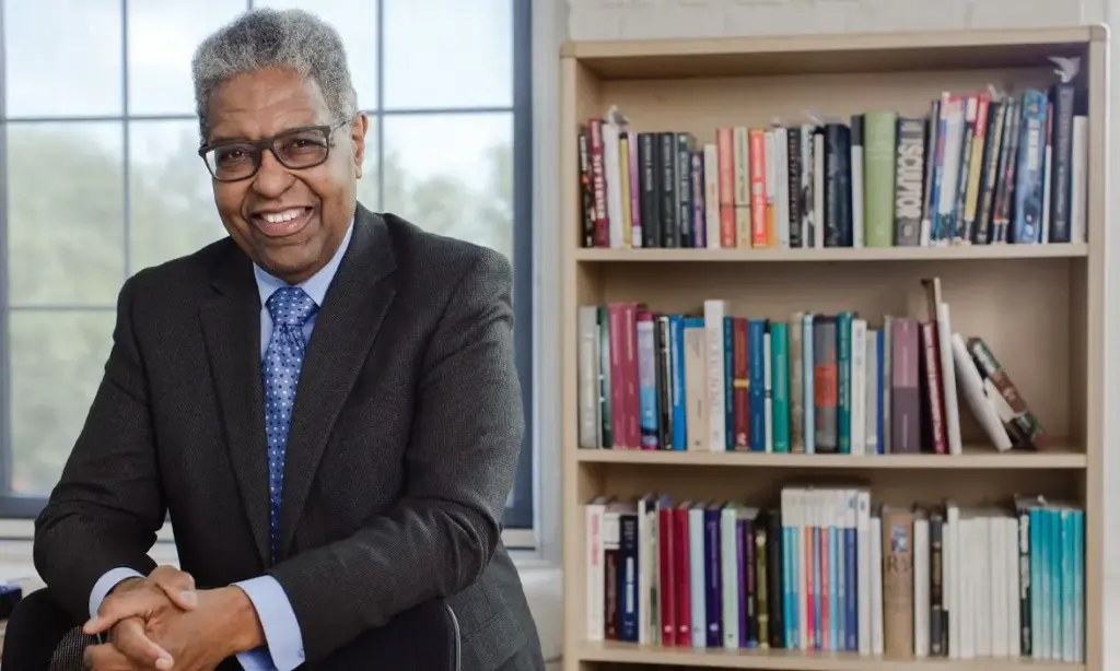 Professional headshot of Dr. William "Sandy" Darity next to a bookshelf full of books