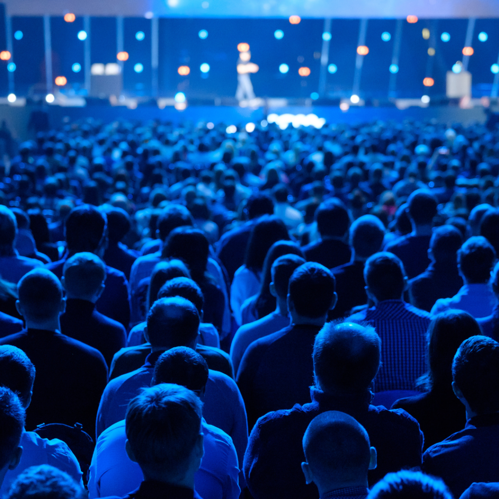 the backs of a crowded audience looking towards a blurred stage