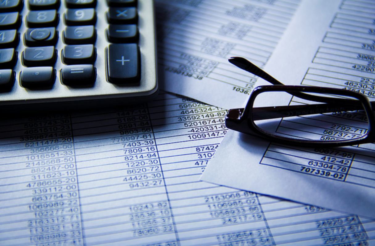 numbers in spreadsheet on piece of paper with a pair of glasses and calculator on top
