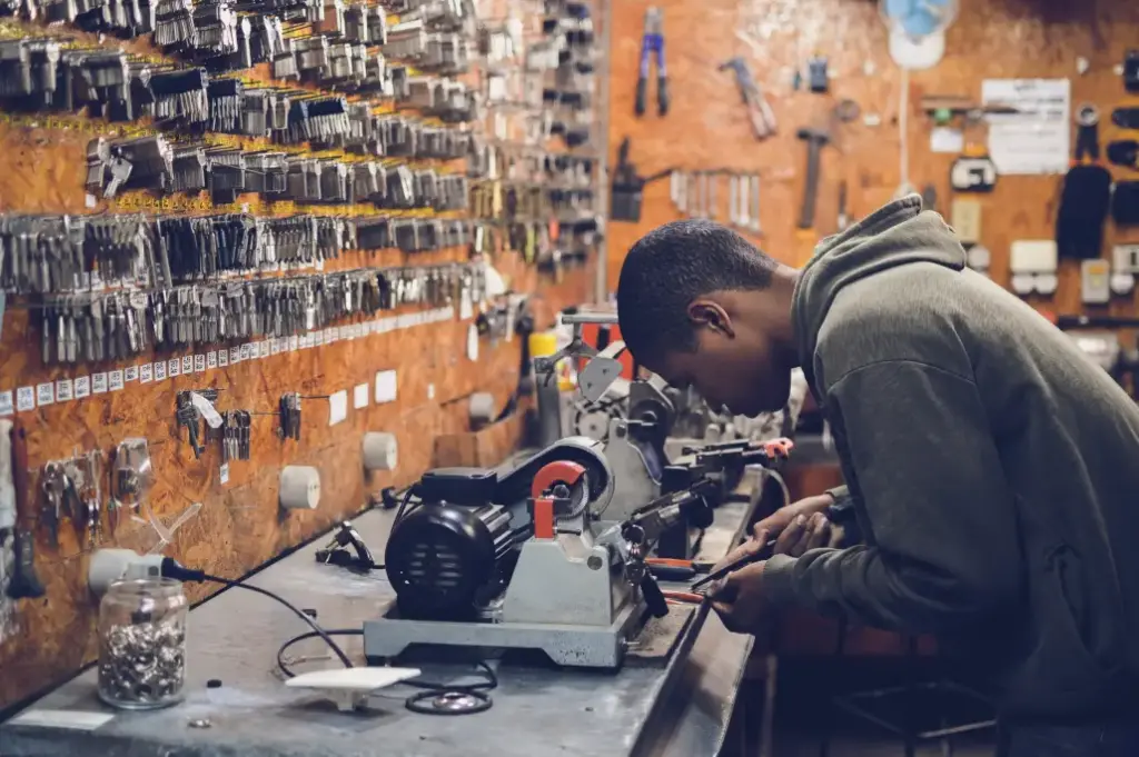 man bent over looking closely at a machine with keys hanging above him