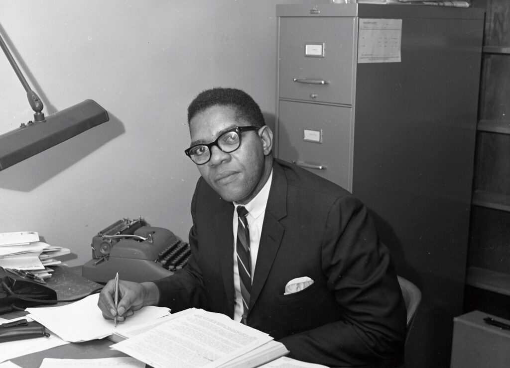 A black and white image of a young Samuel DuBois Cook sitting at a desk