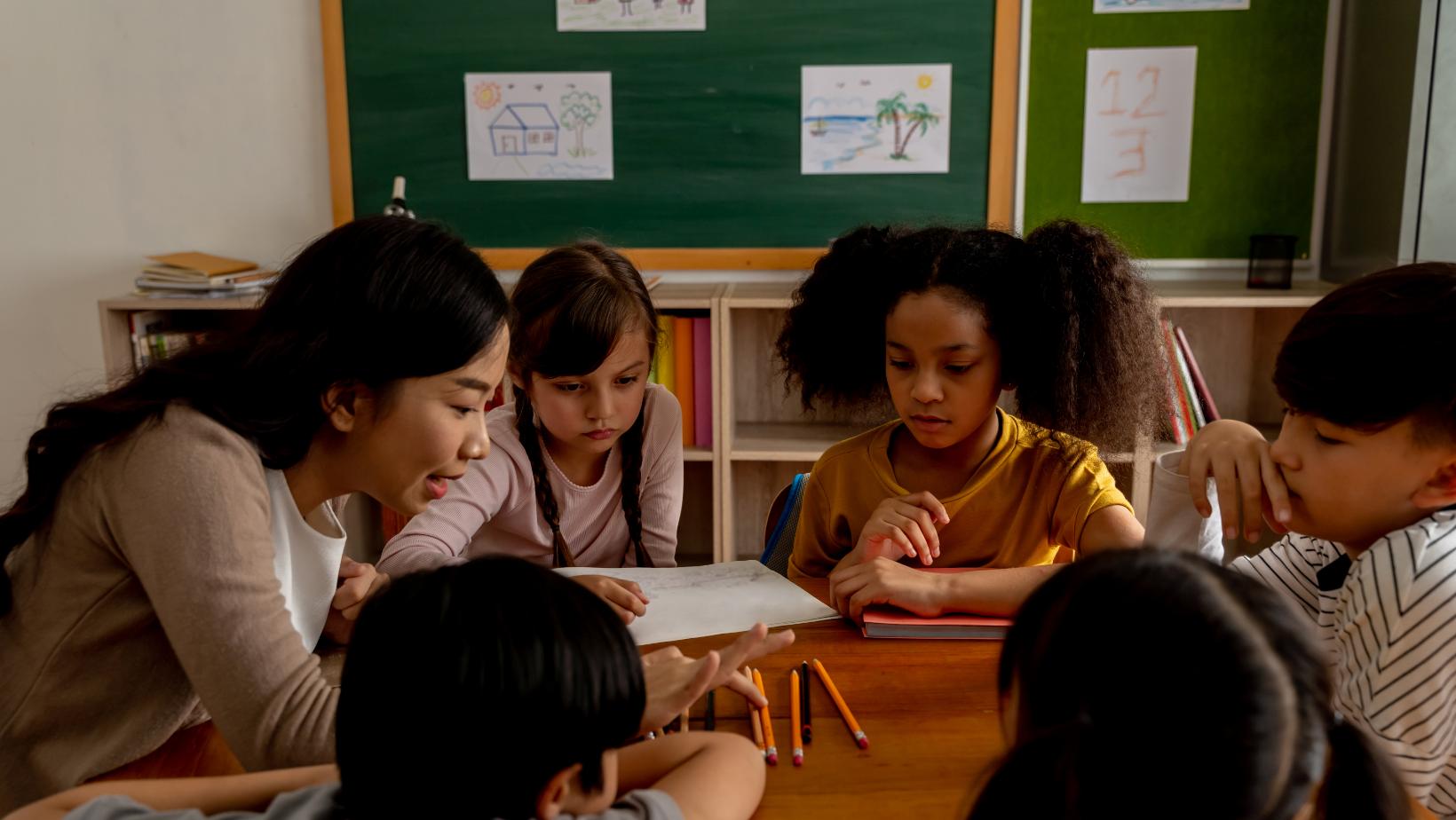 group of children sitting at a table in a circle with teacher